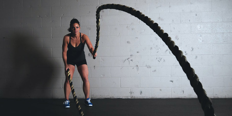 woman wearing black gym clothes holding and training with exercise ropes